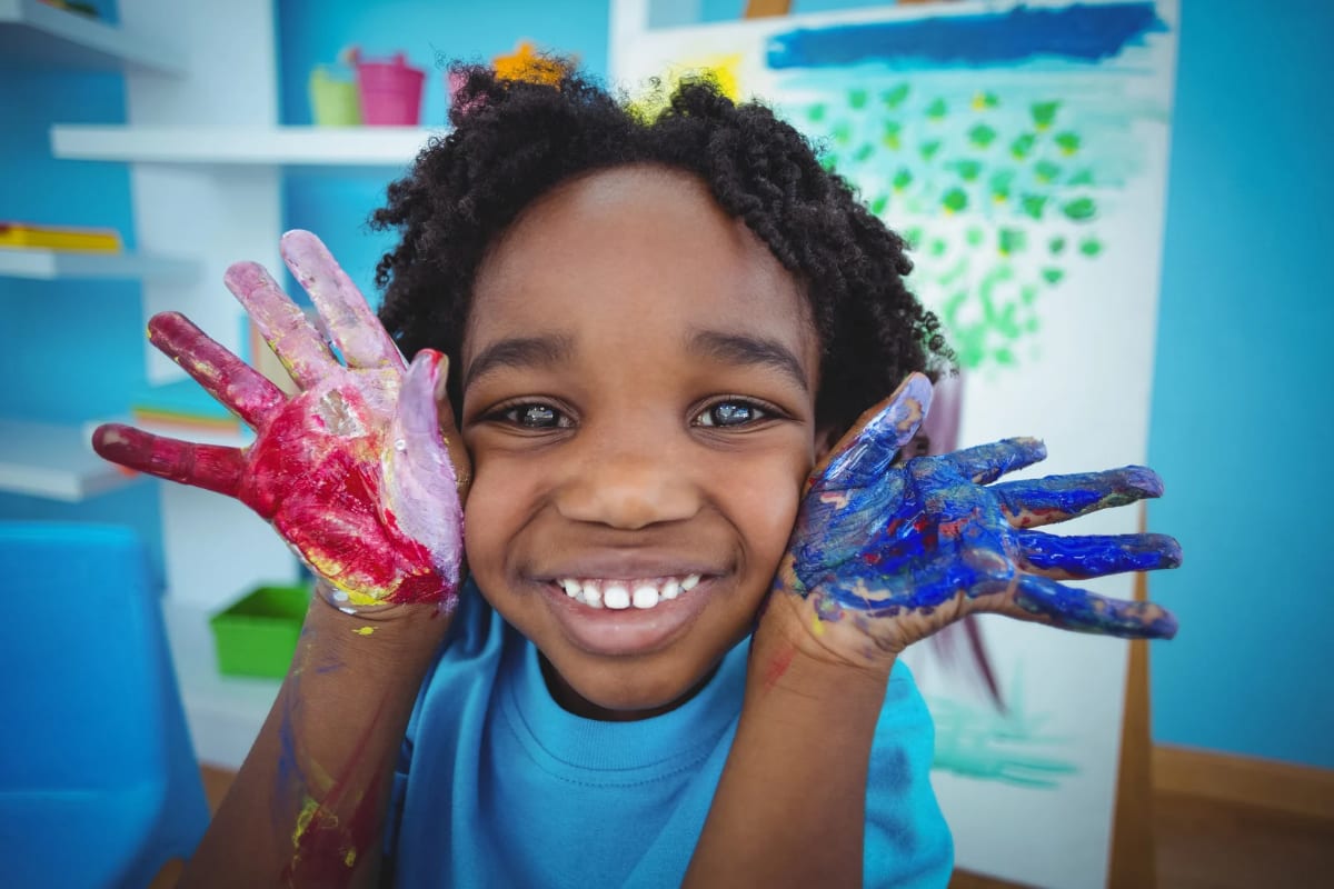 A joyful young child smiling with hands covered in red and blue paint
